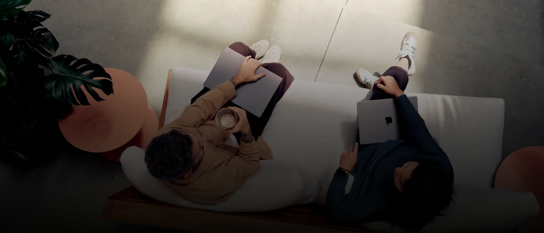 Two colleagues on a sofa with their laptops, seen from above in soft window light